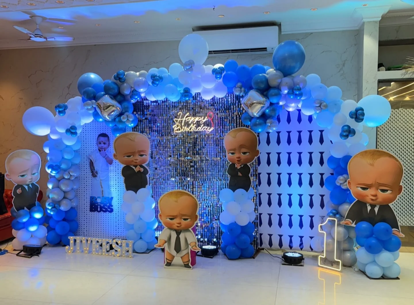 Blue, white and silver balloon arch around a sequin wall with Boss Baby cut-outs