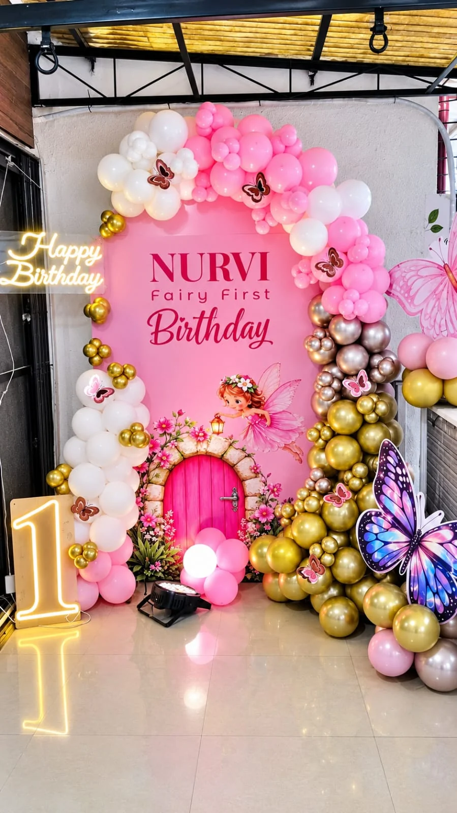 Pink and gold balloon arch around a fairy-door backdrop for a first birthday