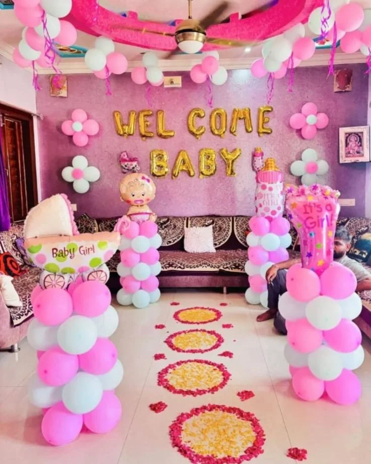 Welcome baby girl home decoration: pink and mint balloon columns, gold foil letters and a petal rangoli path